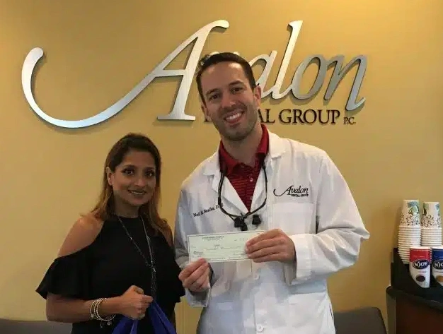 Two people posing together in front of Avalon Dental Group signage in a dental office.