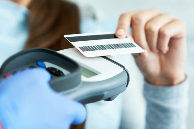 Person holding dental insurance card near payment terminal for dental services