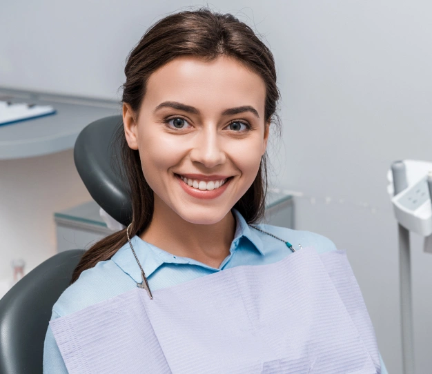 Smiling dental professional in light blue shirt seated in modern dental office setting.