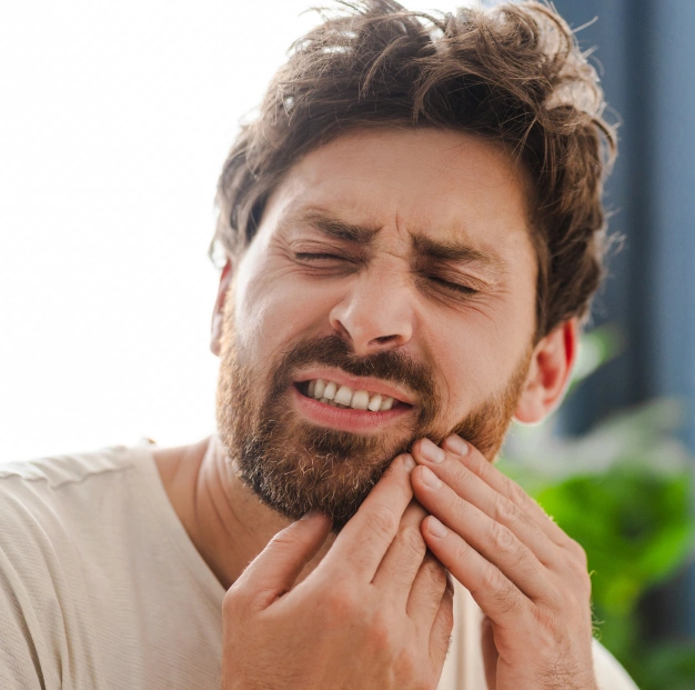 Man experiencing tooth pain, holding cheek with both hands, outdoor setting with blurred background.