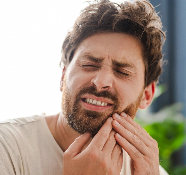 Man holding cheek in pain, touching jaw, wearing light colored shirt indoors