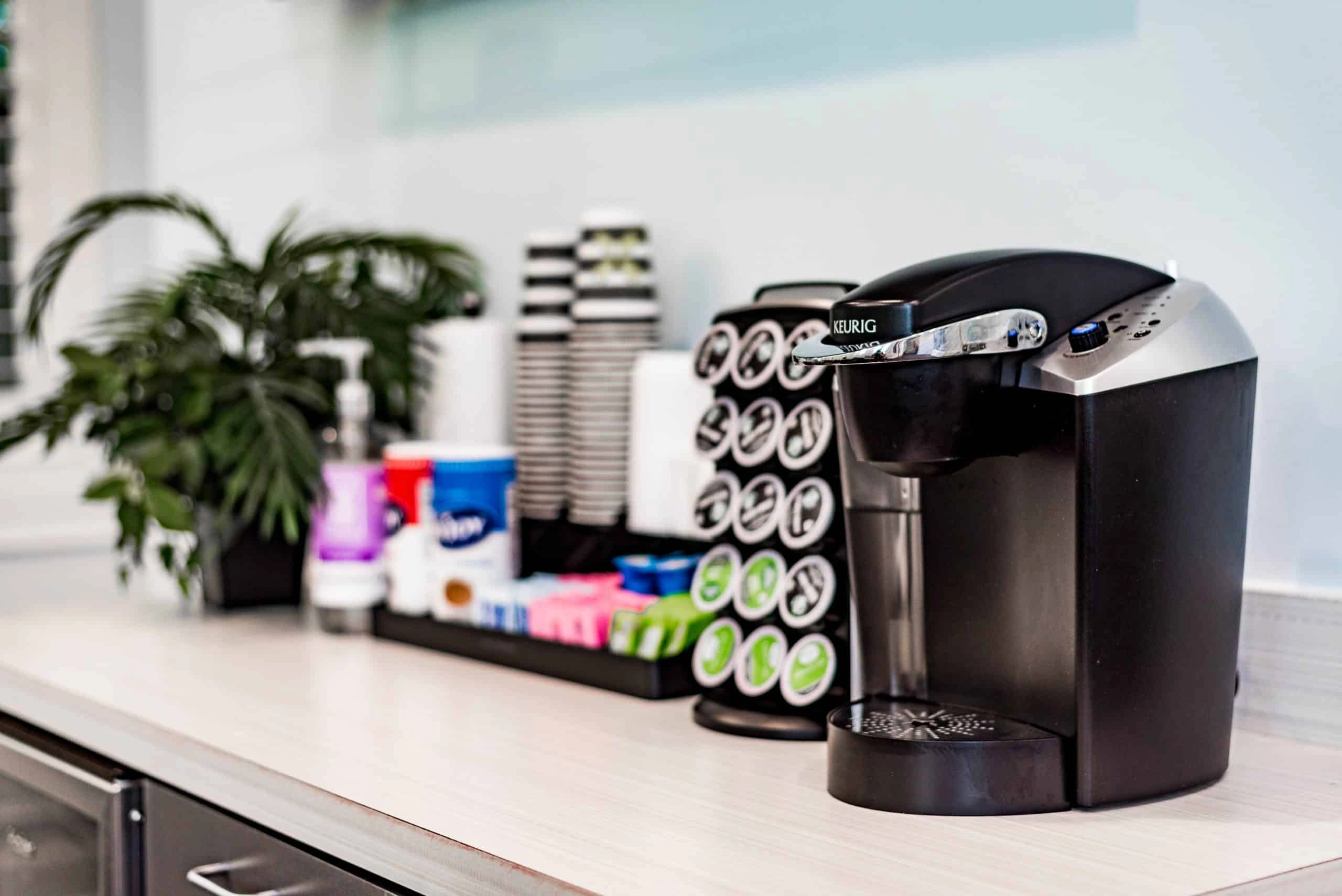 Coffee maker with pods on dental office counter next to plant and supplies