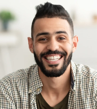 Smiling male dental professional wearing checkered shirt in modern dental office setting.