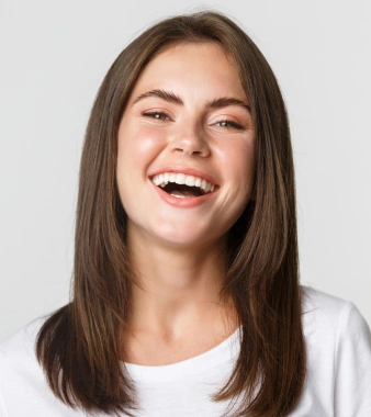 Smiling woman with long brown hair wearing white shirt against neutral background.