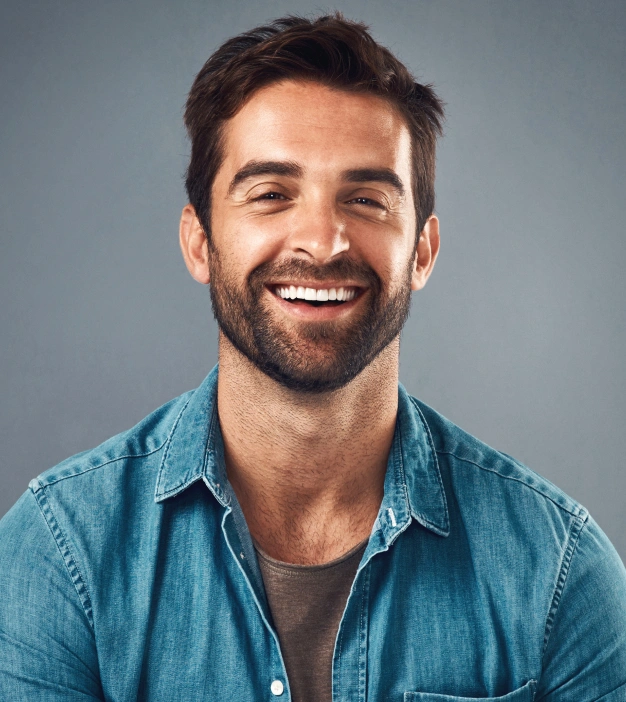 Smiling man in denim shirt against blue background, professional headshot for dental practice