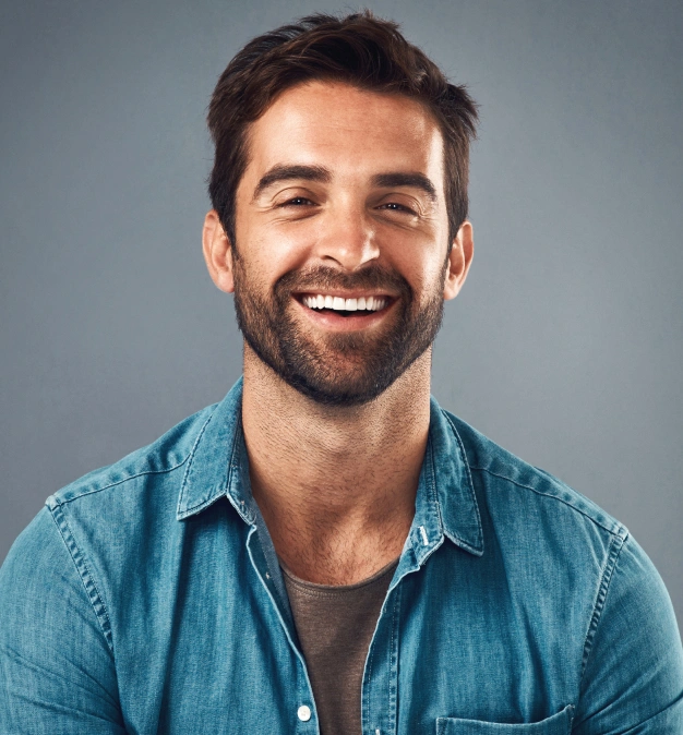 Smiling man in blue shirt against gray background, professional headshot for dental practice.