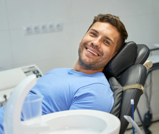 Smiling man in blue shirt relaxing in dental chair at modern dental clinic