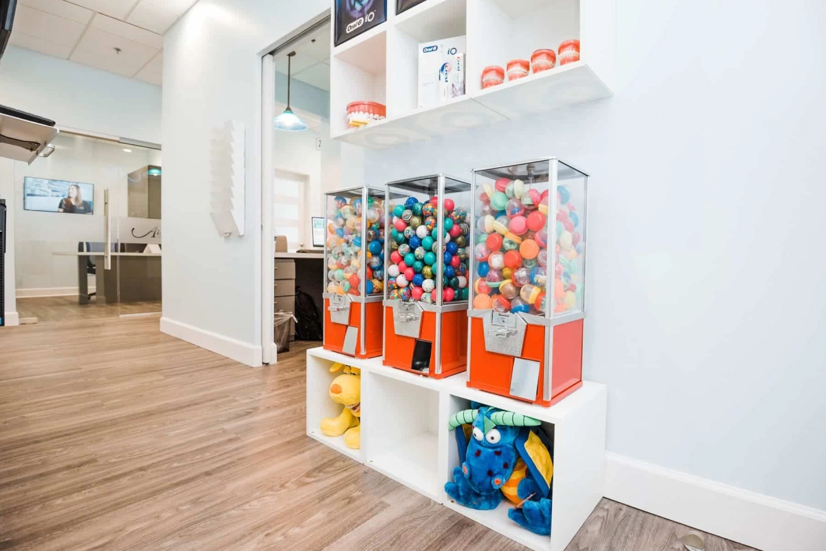 Modern dental office waiting area with white shelving displaying colorful toy dispensers and children's items.