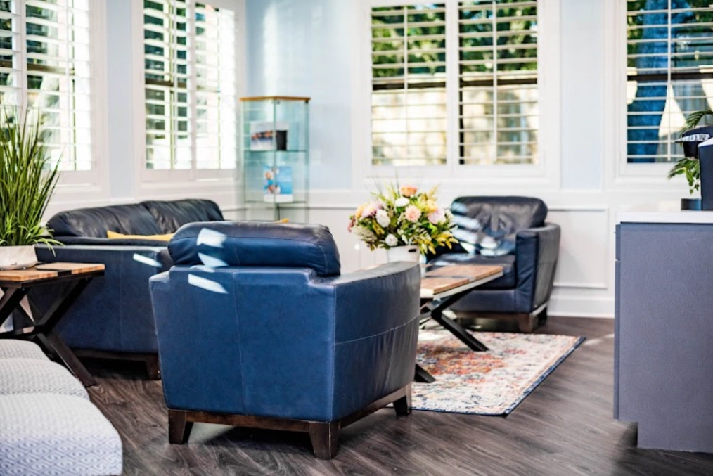 Modern dental office waiting room with blue chairs, natural light, and contemporary furnishings.