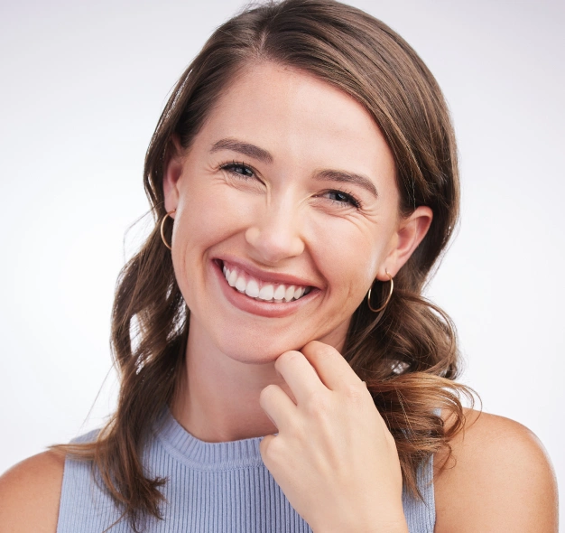 Smiling woman in blue top with hand near face against white background, professional headshot.