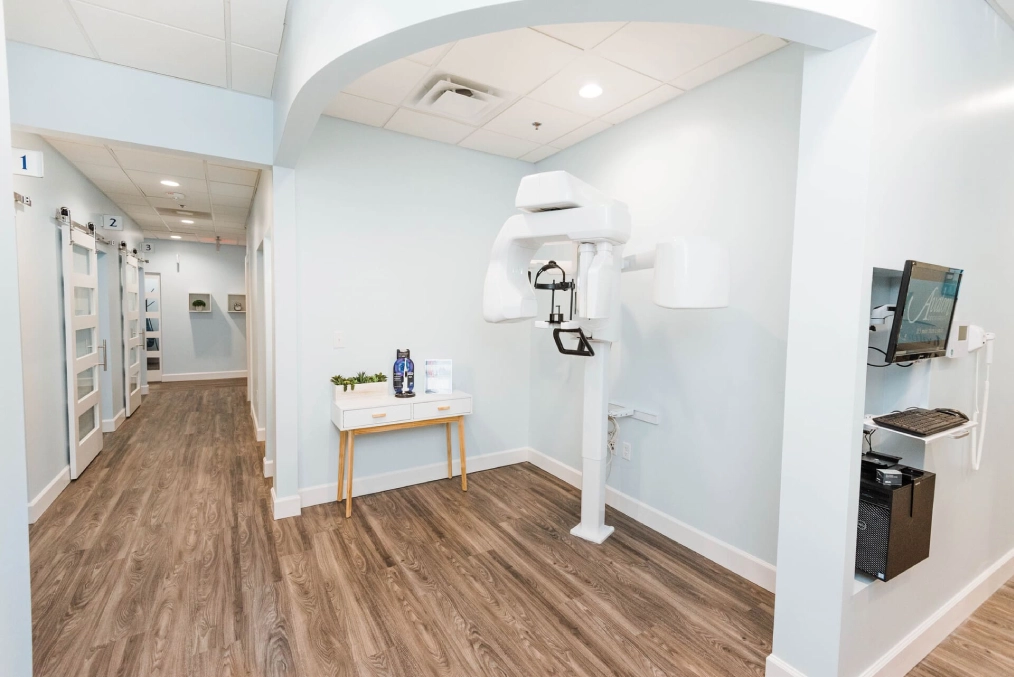 Empty dental operatory with wood flooring, white walls, and modern equipment setup.