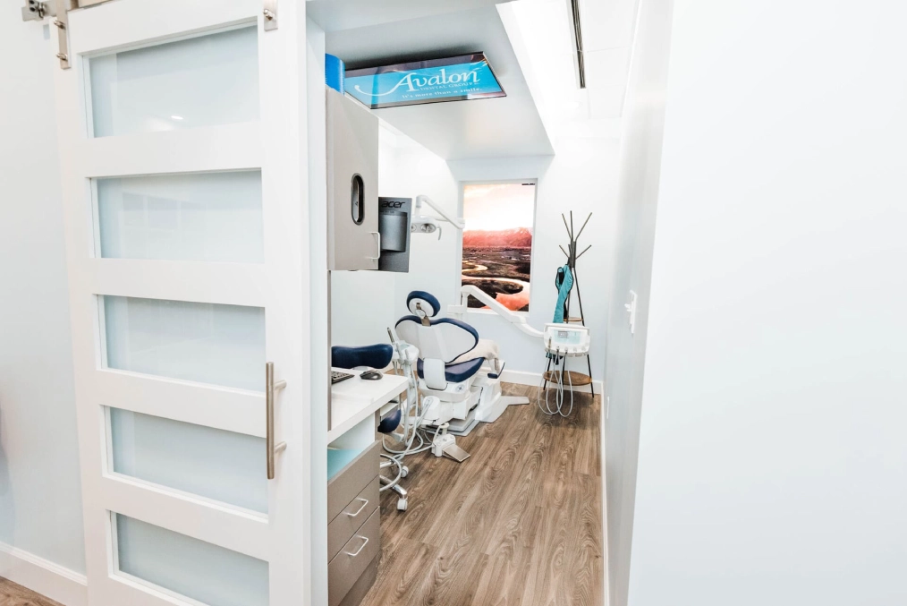 Modern dental office interior with treatment chair visible through open doorway, contemporary white design.