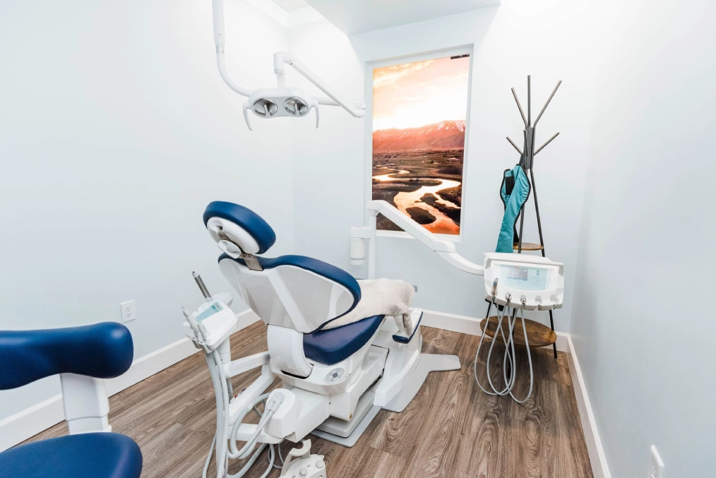 Modern dental treatment room with blue and white chair, overhead light, and minimalist décor.