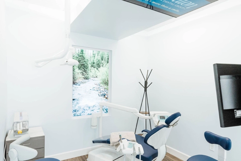 Modern dental treatment room with blue chair, overhead light, and window at Avalon Dental Group