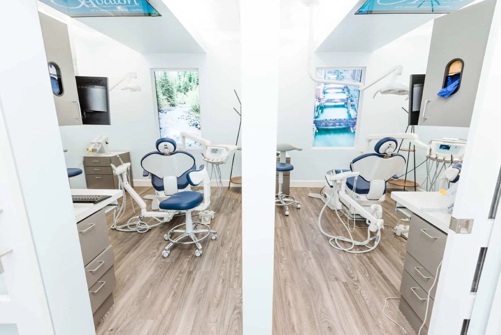 Modern dental treatment room with chair, equipment, and mirror reflections showing clinical setup.