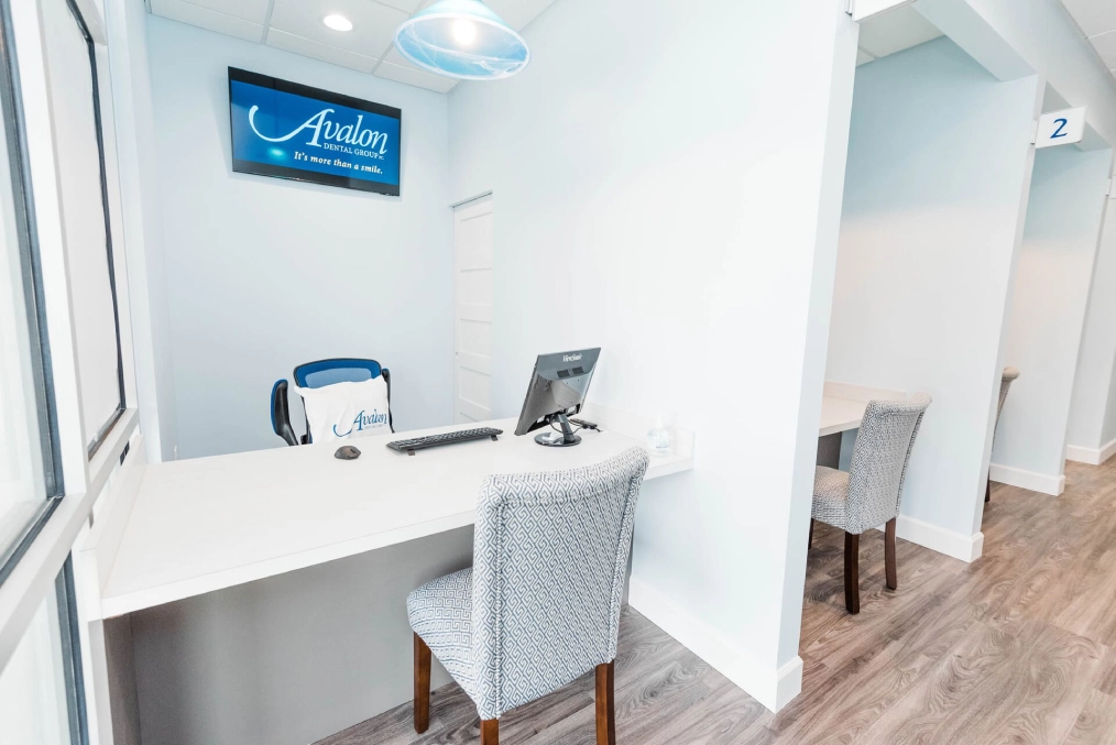 Modern dental office reception area with white desk, computer, and chair in clinical setting.