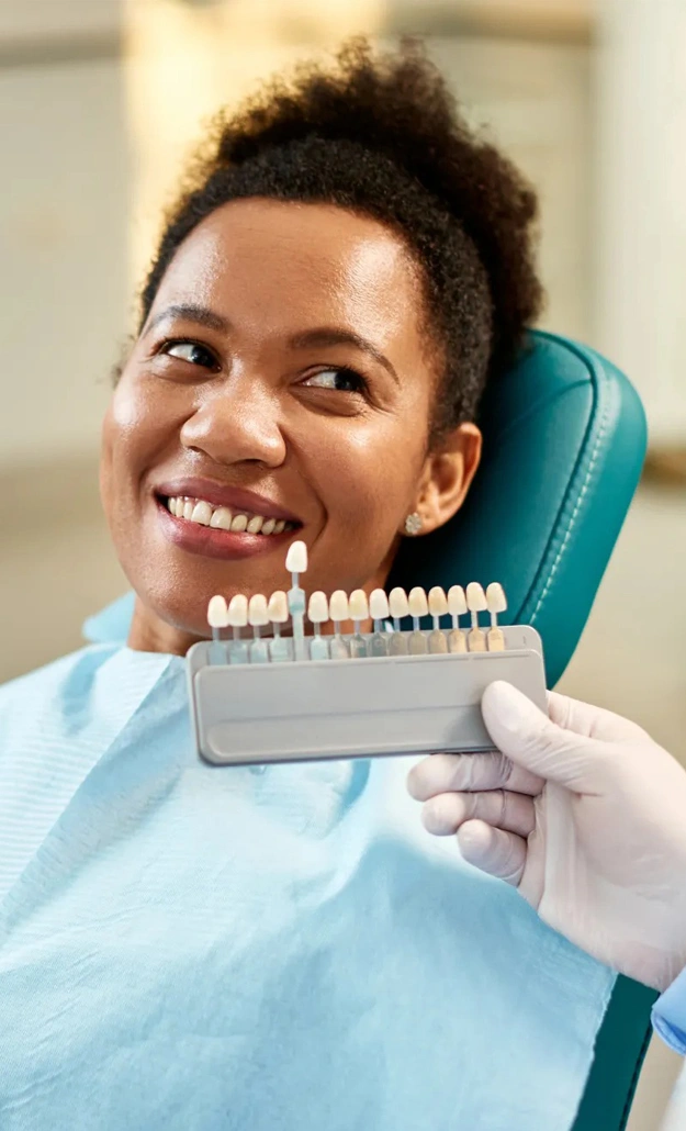 Patient in dental chair smiling while dentist shows tooth shade guide during consultation.