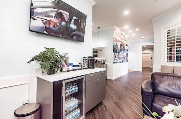 Modern dental office reception area with dark cabinetry, plants, and seating area.