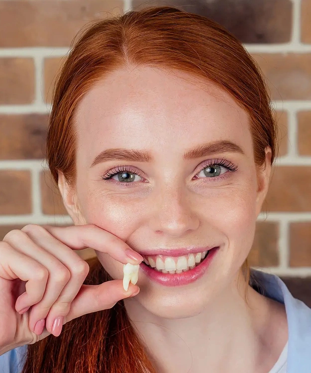Young woman with red hair smiling while flossing teeth against brick background.