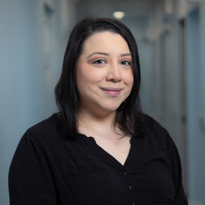 Woman in black shirt smiling at camera in dental office hallway setting.