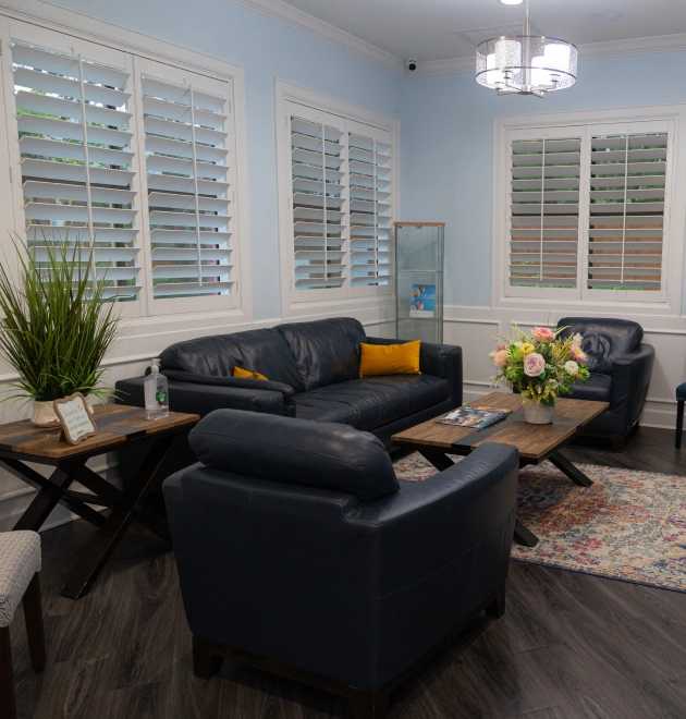 Modern dental office waiting room with blue walls, black leather seating, and white shuttered windows.