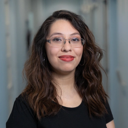 Young woman wearing glasses and black shirt smiles at camera in professional portrait setting.