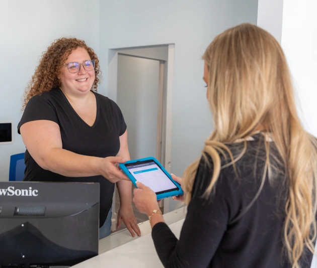 Dental receptionist handing blue card to patient at front desk check-in.