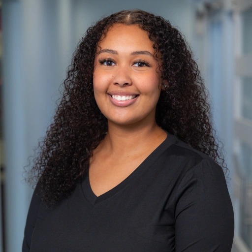 Professional headshot of smiling woman with long curly hair wearing black v-neck shirt against blurred background.