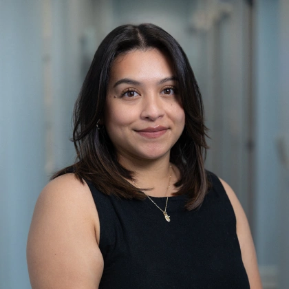 Woman smiling at camera in professional headshot against blue background for dental practice.