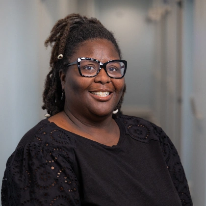 Woman wearing glasses and black sparkly top smiles at camera in professional indoor setting.