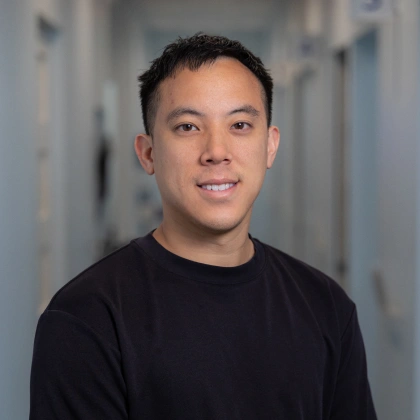 Asian man smiling at camera wearing black shirt in clinical hallway setting.