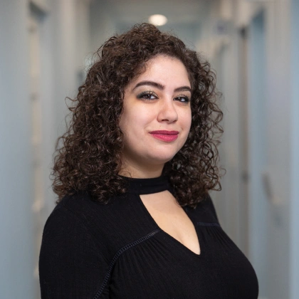 Woman with curly brown hair smiling in black top, dental office hallway setting.
