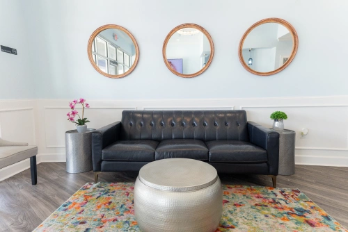 Modern dental office waiting room with dark gray sofa, round mirrors, and colorful area rug.