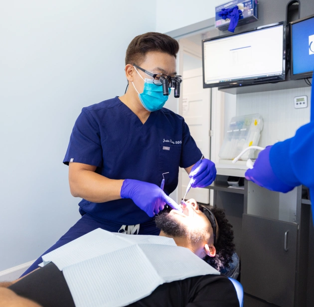 Dentist in blue scrubs and mask performing dental procedure on patient in clinical setting.