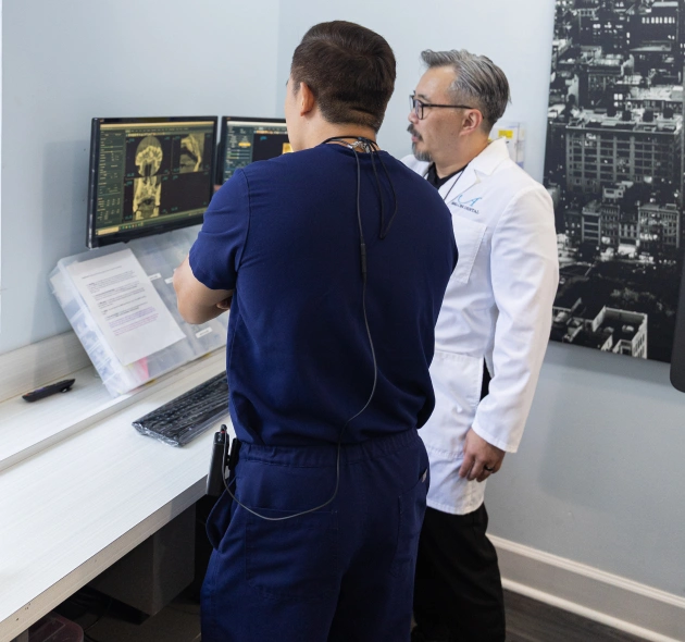Two men reviewing dental imaging scans at a computer workstation in a clinical office.