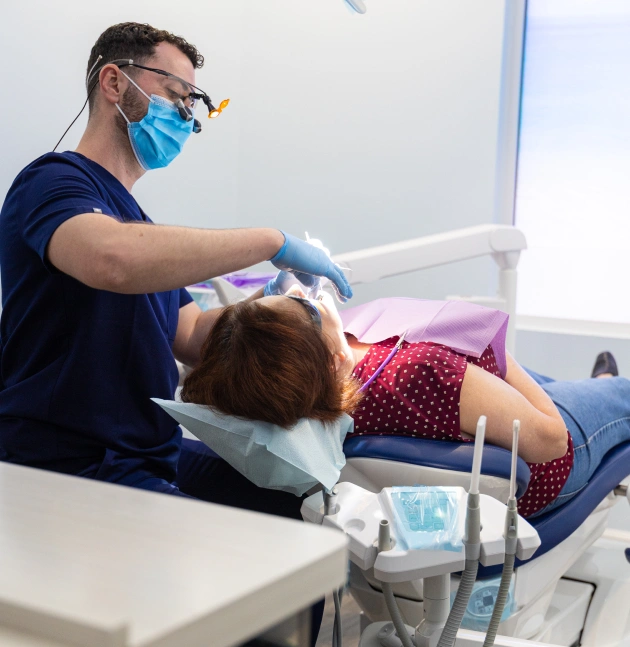 Dentist in blue mask and gloves examining young patient in dental chair at Avalon Dental Group clinic.