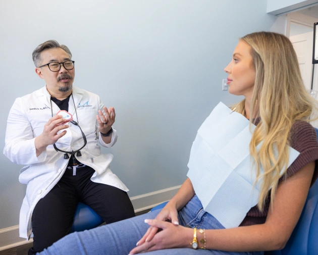 Dentist in white coat consults with female patient in clinical examination room.