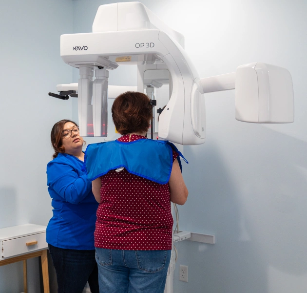 Dental professional in blue scrubs positioning patient for panoramic X-ray scan at Avalon Dental Group clinic.
