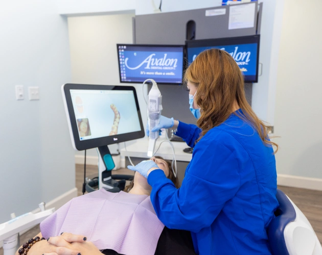 Dental professional in blue scrubs performing ultrasound examination on patient in clinical setting.