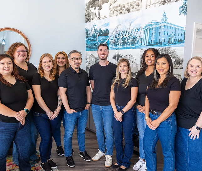 Avalon Dental Group team of twelve staff members posing together in office wearing black shirts and jeans