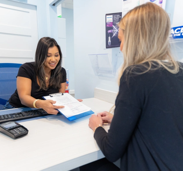 Dental receptionist assisting patient at front desk with paperwork in modern office.