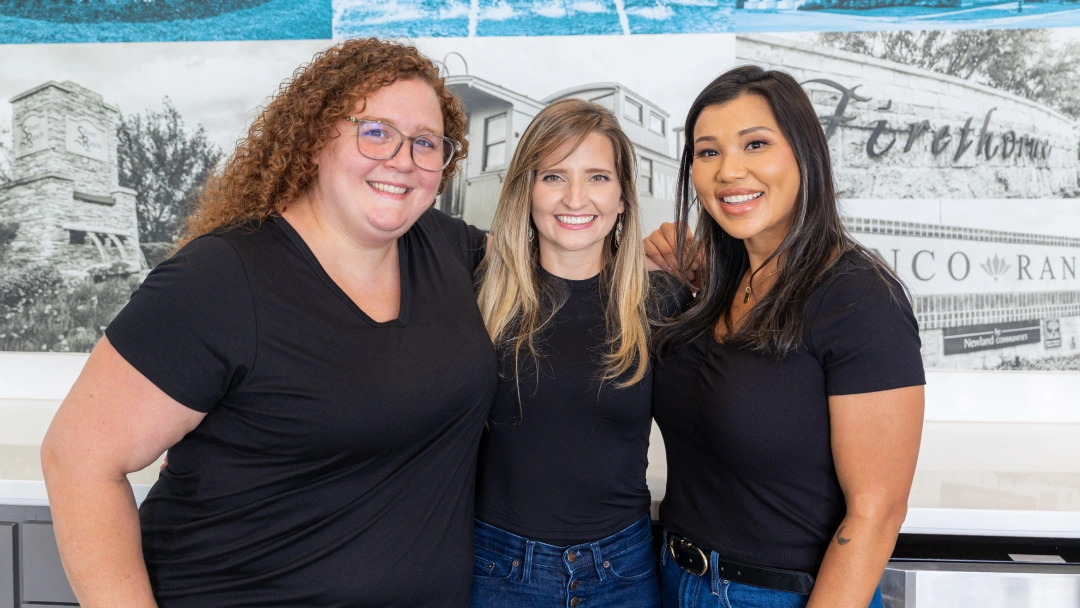 Three women smiling at camera in dental office with blue water background