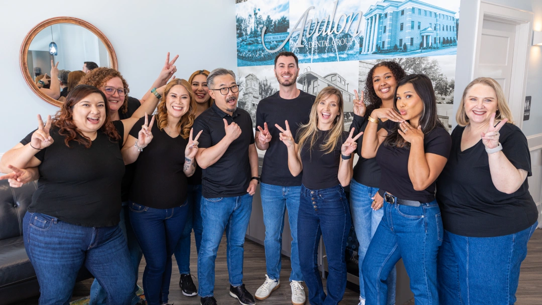 Avalon Dental Group team members in dark shirts and jeans giving thumbs up in office setting.
