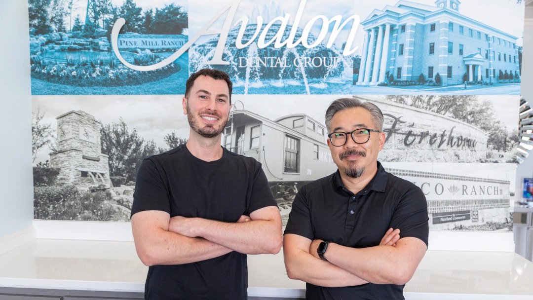 Two male dental professionals posing with crossed arms in front of Avalon Dental Group office backdrop.
