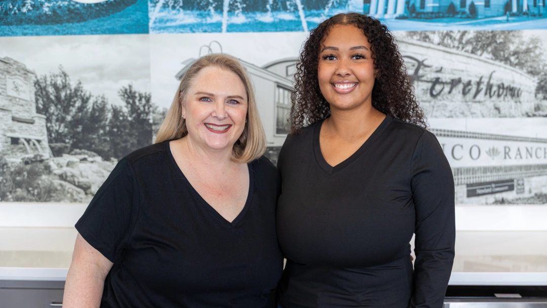 Two women smiling at camera in front of Avalon Dental Group branded backdrop.