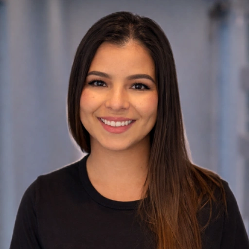 Young woman smiling at camera in professional portrait against blurred office background.