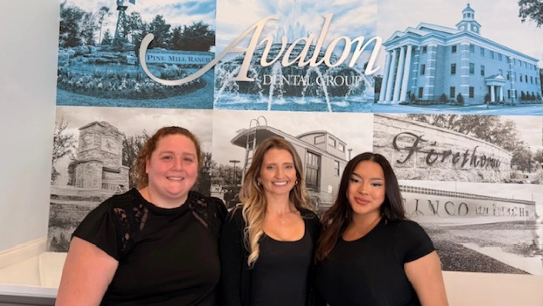 Three dental professionals posing together in front of Avalon Dental Group branded backdrop with architectural images.