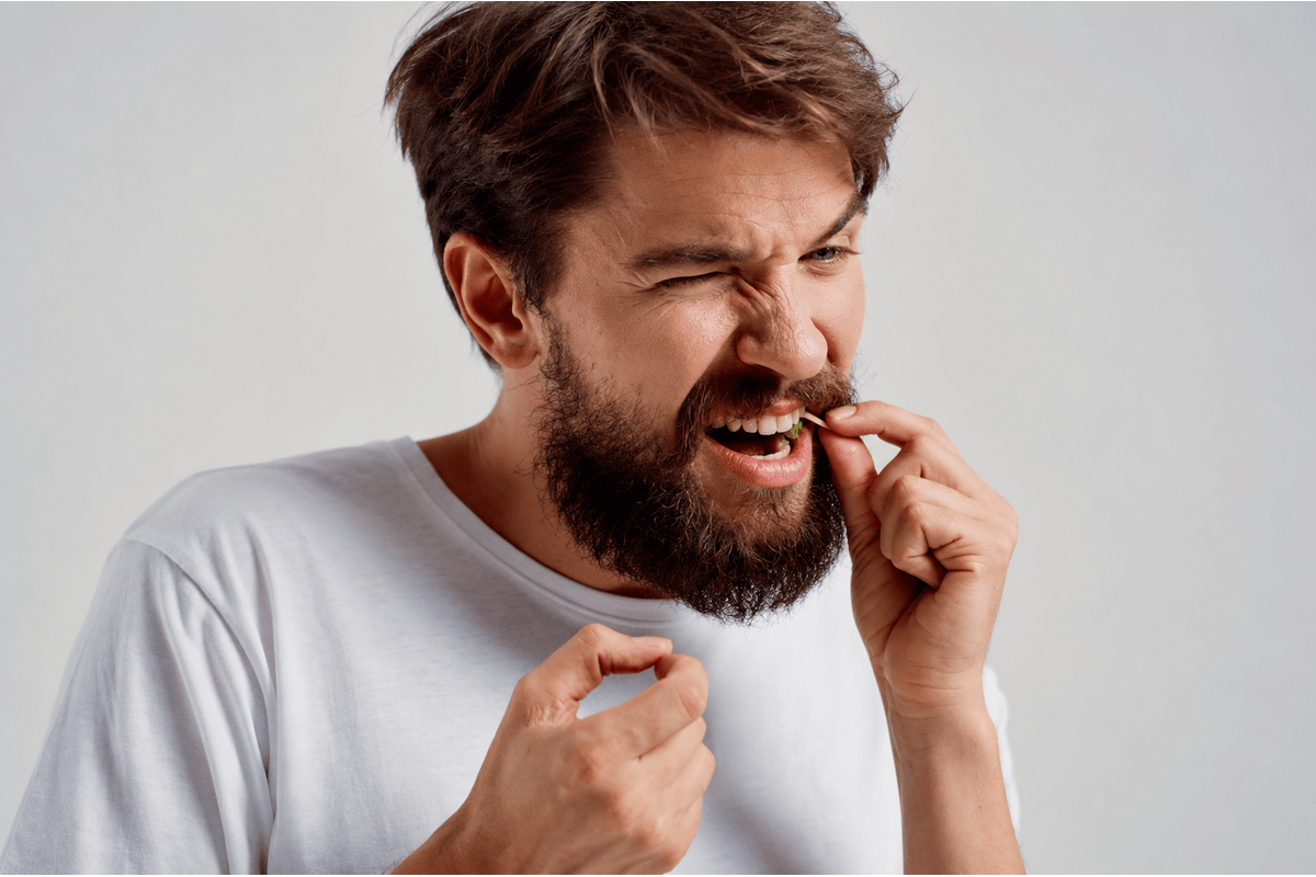 Adult man experiencing discomfort from food trapped between two teeth
