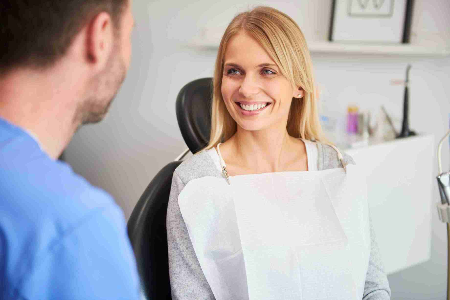 Woman smiling while discussing dental insurance coverage with a dentist in an office setting.
